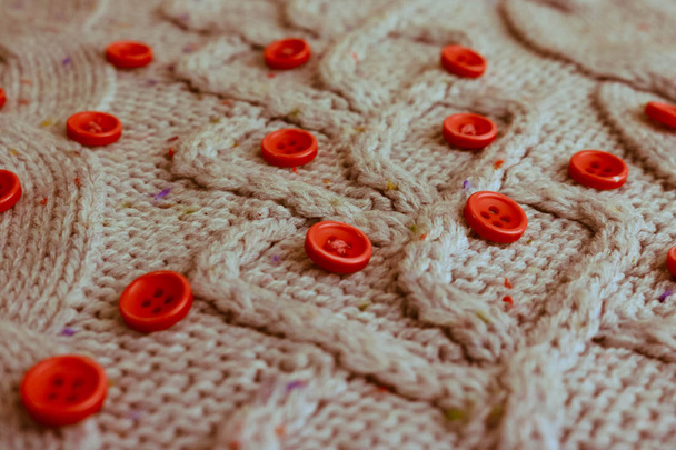 schöne Textur eines weichen warmen natürlichen Pullovers mit einem Strickmuster aus Garn und roten kleinen runden Knöpfen zum Nähen. der Hintergrund - Foto, Bild