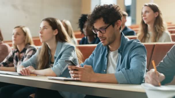 Spaanse Man gebruik Smartphone terwijl ze op een lezing in de klas. Collegezaal gevuld met studenten die studeren. Jongeren aan de Universiteit. - Video
