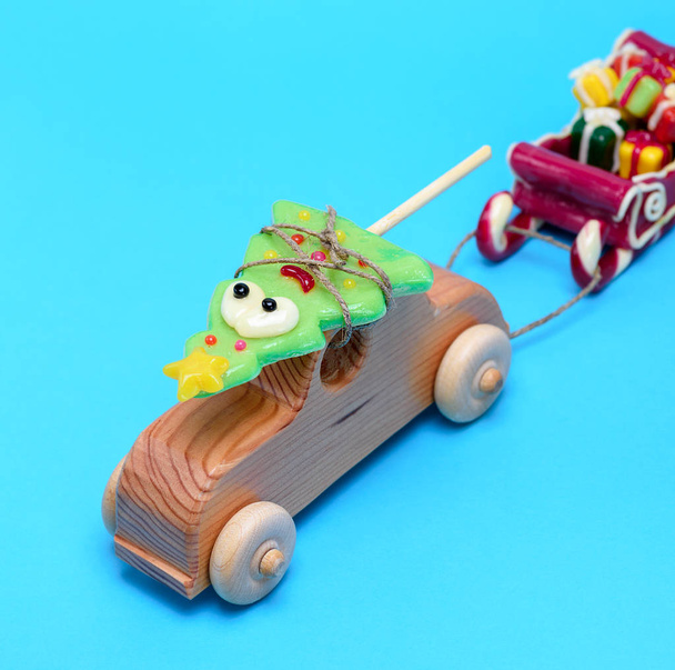 coche infantil de madera lleva un abeto de vacaciones de caramelo y tira de un trineo con regalos sobre un fondo azul
 - Foto, Imagen