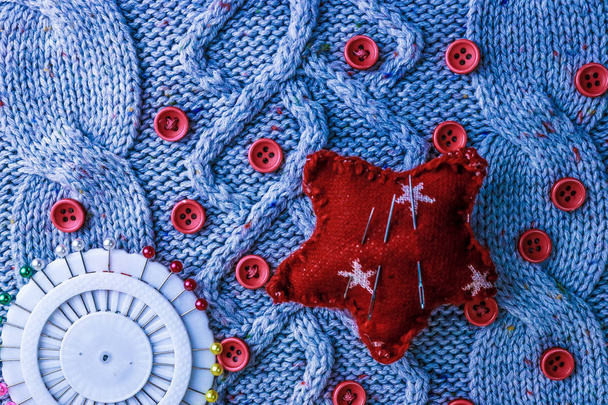 Bela textura de um suéter natural quente suave, tecidos tricotados e pequenos botões redondos vermelhos de costura e uma almofada de agulha. Deitado. O fundo
 - Foto, Imagem