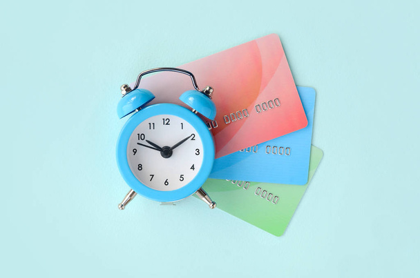 Malý modrý budík leží na barevné kreditní karty. Pojem moderní rychlé online bankovnictví a rychle finančních operací - Fotografie, Obrázek
