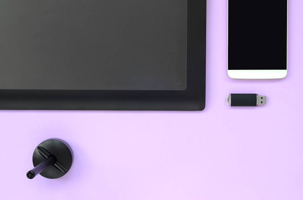 Grafik-Tablet und Stift für Illustratoren und Designer liegt mit USB-Speicherkarte und Smartphone auf pastellviolettem Hintergrund. flach lag Minimalismus. Ansicht von oben - Foto, Bild