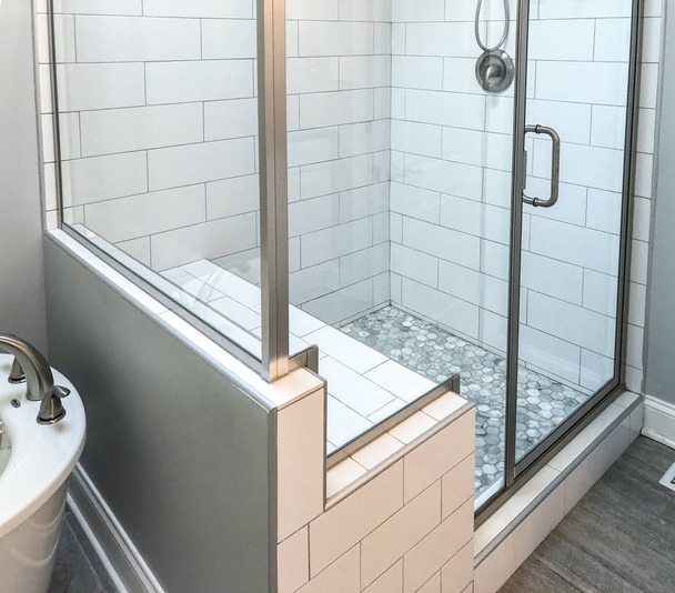 Bathroom shower base with white rectangular wall tiles, custom shower seat, mosaic floor tiles inside shower base and brownish floor tile. Glass shower doors and panels with chrome bathroom fixtures  - Photo, Image