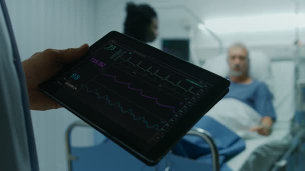 In het ziekenhuis arts houdt tabletcomputer tekenen Vital van een Senior patiënt in Bed liggen. Verpleegster doet Checkup. Moderne geriatrie Ward. - Video