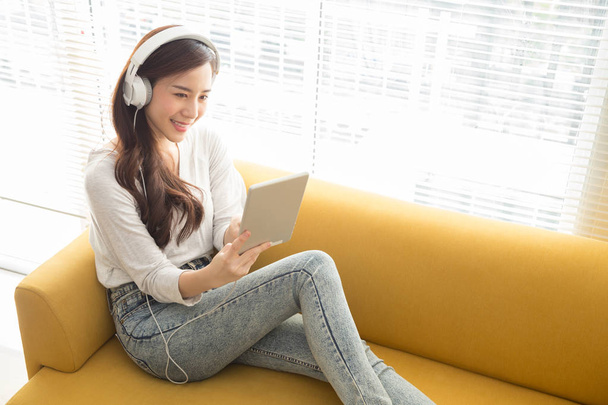 Hermosa mujer asiática joven escuchando música con auriculares utilizando una tableta en la habitación, Adolescente disfrutando de la parte superior gráfico servicio de streaming de música en el sitio web con su lista de reproducción, Relájese y concepto de ocio
 - Foto, Imagen