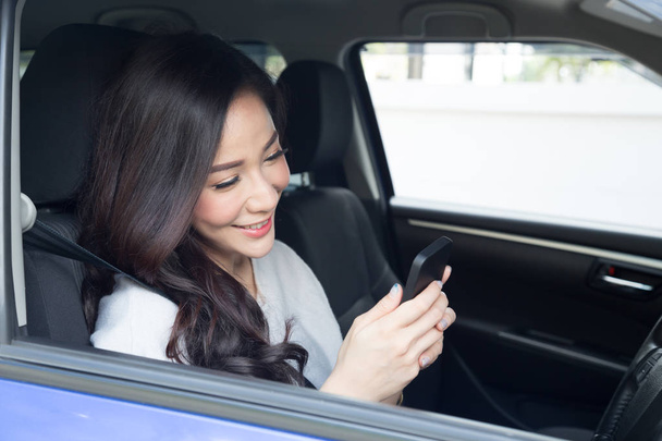Młody piękny Asian kobieta uśmiechając się siedząc na siedzenia kierowcy w samochodzie i za pomocą smartfona z mobilnej nawigacji gps aplikacja lub mapę, dotknij ekranu i czytanie wiadomości czatu lub sieci społecznej - Zdjęcie, obraz