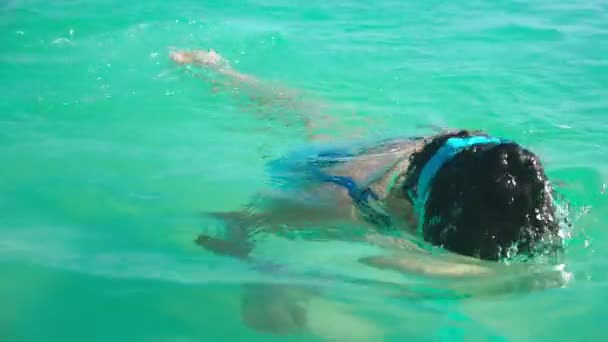 ευτυχισμένος κορίτσι σε μια μάσκα κολύμπι αναδύεται από τα καθαρά νερά της θάλασσας, εξετάζει τη φωτογραφική μηχανή και χαμόγελα - Πλάνα, βίντεο