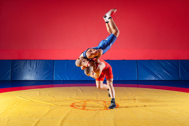 Dwa grecko-rzymskiego zapaśników w czerwony i niebieski mundur wrestling na żółty wrestling dywan w siłowni. Pojęcie godziwej wrestling - Zdjęcie, obraz