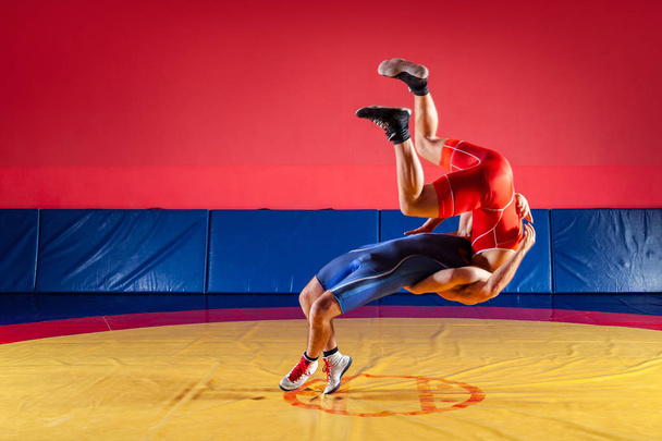 El concepto de lucha libre justa. Dos luchadores greco-romanos en uniforme rojo y azul luchando en una alfombra de lucha libre amarilla en el gimnasio
 - Foto, Imagen