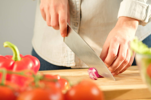 Girl cuts red onions for vegetable salad. Cooking salad - Fotó, kép