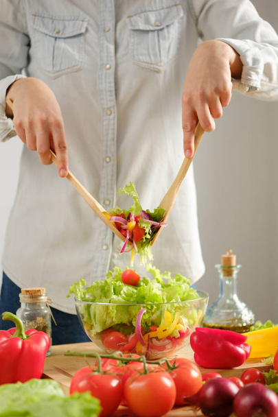 Girl interferes with vegetable salad. Cooking salad - 写真・画像