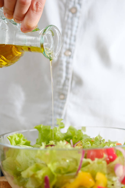 Girl pours olive oil into vegetable salad. Cooking salad - Fotografie, Obrázek