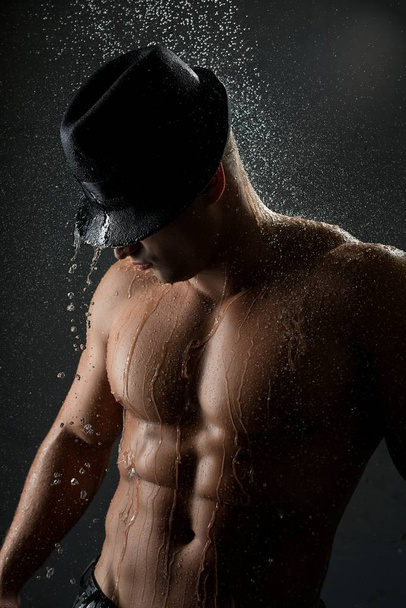 Young muscular man in shower in the dark - Фото, изображение