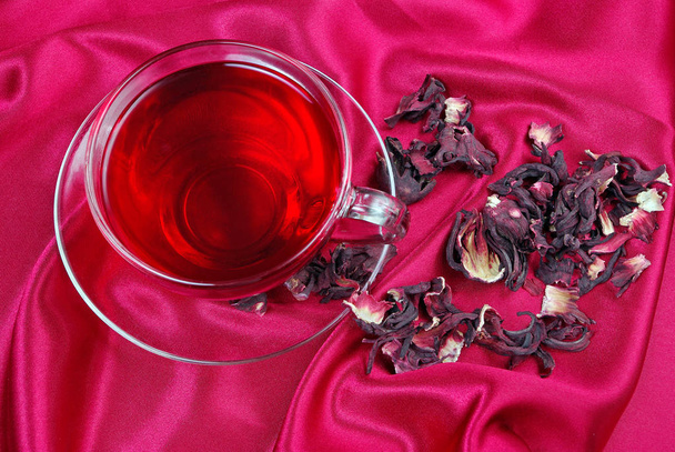 φλιτζάνι τσάι ιβίσκου σε φόντο κόκκινο μετάξι. το Top view. θεραπεία της γρίπης και του κρυολογήματος - Φωτογραφία, εικόνα