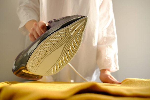 Girl ironing clothes  at home a yellow jacket  - Fotó, kép