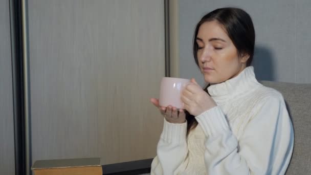 schönes Mädchen trinkt Tee und liest ein Buch auf dem Sofa - Filmmaterial, Video