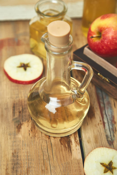 Ocet jabłkowy cydr. Szklana butelka z organicznych ocet jabłkowy na drewnianym stole. Zdrowy napój ekologicznej żywności. Butelka z świeży cydr w pobliżu jesiennych jabłek. Rustykalne tło, miejsca na tekst - Zdjęcie, obraz