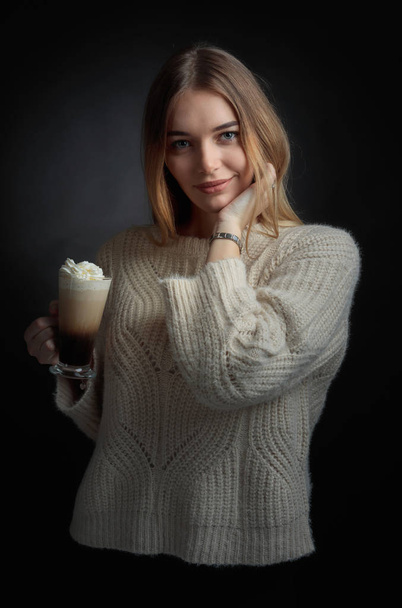 Привлекательная молодая женщина с ирландским кофе. Красивая блондинка в свитере держит кружку кофе со сливками
. - Фото, изображение
