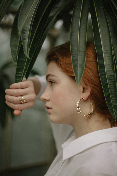 sensuale donna dai capelli rossi in camicia bianca in posa tra piante verdi
  - Foto, immagini