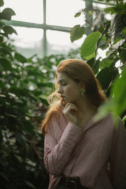 緑の植物の間でポーズのストライプのシャツで官能的な若い女性  - 写真・画像