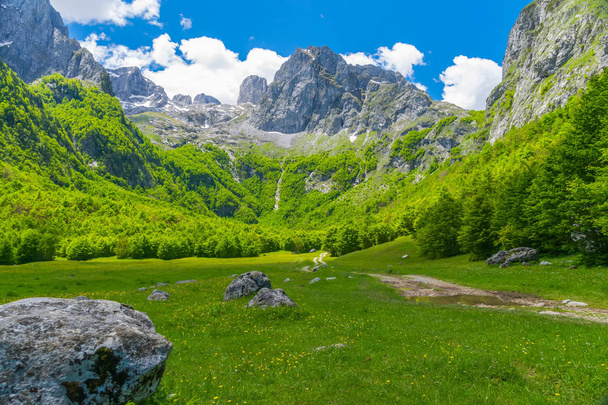 Vista panorámica del camino de tierra a través de una pintoresca llanura entre altas montañas
 - Foto, Imagen
