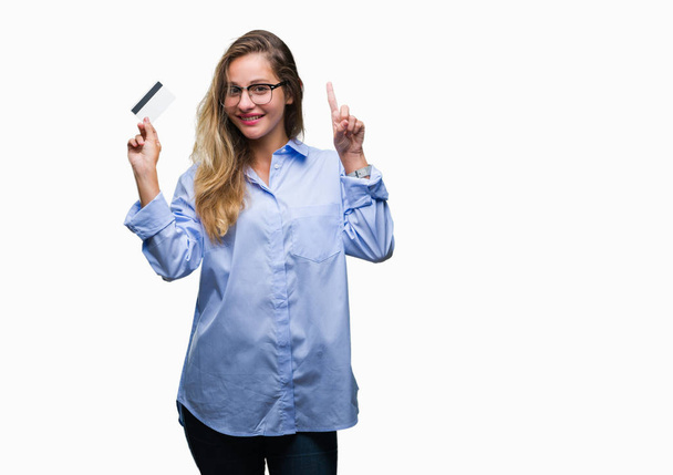 Young beautiful blonde woman holding credit card over isolated background surprised with an idea or question pointing finger with happy face, number one - Φωτογραφία, εικόνα
