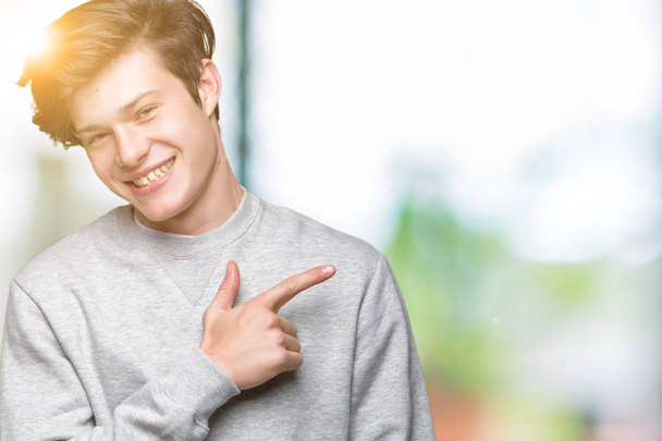 Young handsome sporty man wearing sweatshirt over isolated background cheerful with a smile of face pointing with hand and finger up to the side with happy and natural expression on face - Photo, Image
