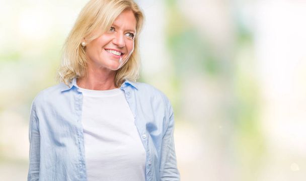 Middle age blonde woman over isolated background looking away to side with smile on face, natural expression. Laughing confident. - Foto, Bild