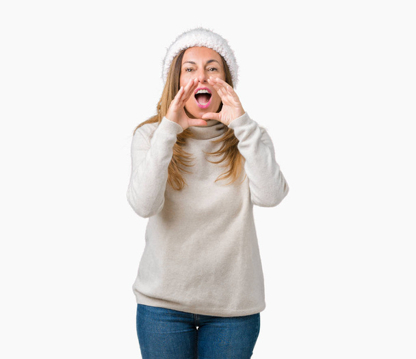 schöne Frau mittleren Alters trägt Winterpullover und Hut über isoliertem Hintergrund schreit wütend laut mit den Händen über dem Mund - Foto, Bild