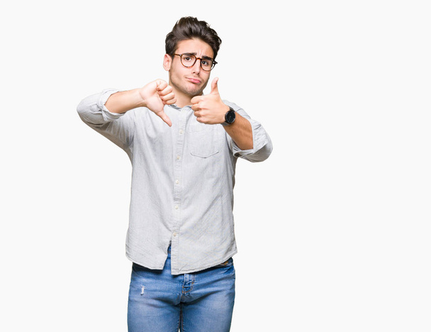 Молодий красивий чоловік носить окуляри над ізольованим тлом Робить великі пальці вгору і вниз, розбіжності і вираз згоди. Божевільний конфлікт
 - Фото, зображення