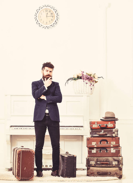 Macho elegant on thoughtful face standing near pile of vintage suitcase. Luggage and travelling concept. Man, traveller with beard and mustache with luggage, luxury white interior background - Φωτογραφία, εικόνα