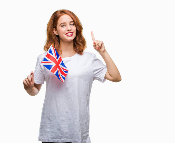 幸せそうな顔、ナンバーワンのアイデアや質問ポインティング指と分離の背景の上イギリスの旗を保持している若い美しい女性を驚かせた - 写真・画像