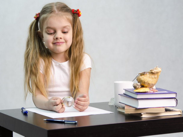 Девушка задумчиво и без усилий поворачивает стеклянный глобус, сидя за столом по образу писателя
 - Фото, изображение