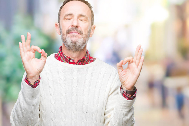 Edad media hoary hombre mayor con suéter de invierno sobre fondo aislado relajarse y sonreír con los ojos cerrados haciendo gesto de meditación con los dedos. Concepto de yoga
. - Foto, imagen