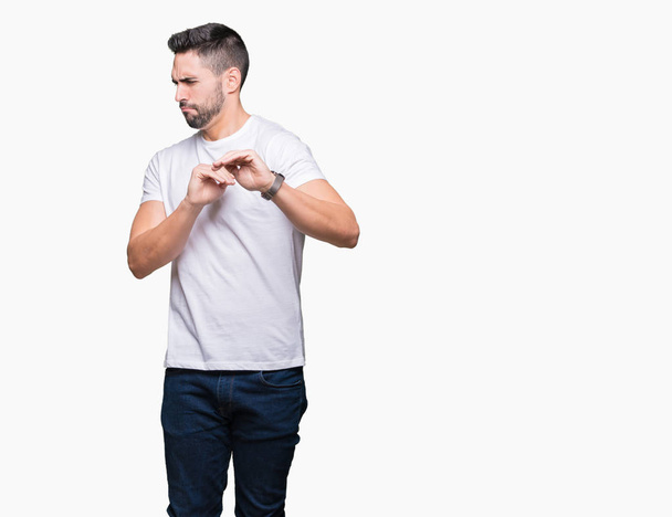 junger Mann in lässigem weißen T-Shirt über isoliertem Hintergrund angewiderte Miene, ungehalten und ängstlich dabei Ekel Gesicht, weil Abneigung Reaktion. mit erhobenen Händen. Ärgerliches Konzept. - Foto, Bild