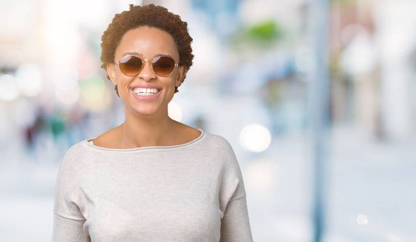 Gyönyörű fiatal afrikai-amerikai nő, napszemüveget visel, mint elszigetelt háttér egy boldog és hűvös mosollyal az arcán. Szerencsés személy. - Fotó, kép