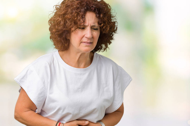 Beautiful middle ager senior woman wearing white t-shirt over isolated background with hand on stomach because indigestion, painful illness feeling unwell. Ache concept. - Photo, image