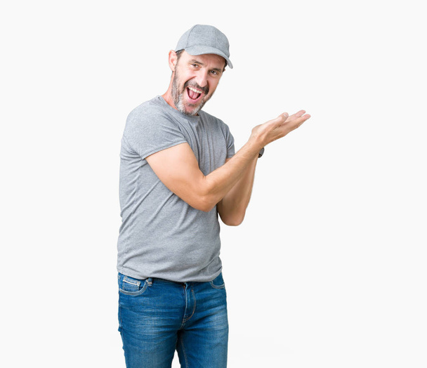 Brunetě středního věku otřepané starší muž nosí sportovní čepice přes samostatný pozadí ukazující na boku s rukou a otevřené dlaně, představující, reklama se šťastná a věří - Fotografie, Obrázek