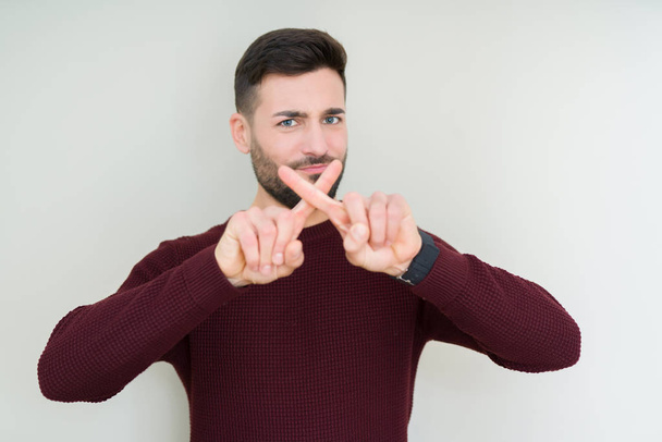 junger gutaussehender Mann trägt einen Pullover über isoliertem Hintergrund Ablehnung Ausdruck Daumendrücken tut negatives Zeichen - Foto, Bild