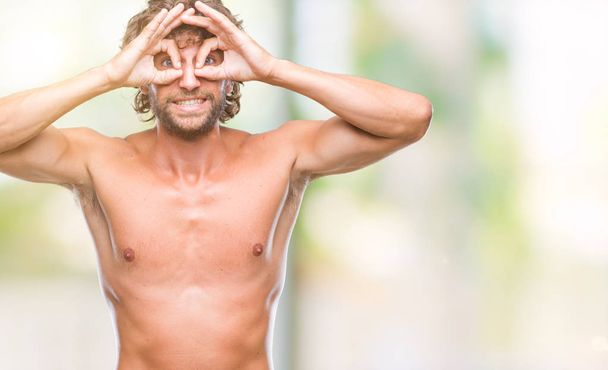 Handsome hispanic model man sexy and shirtless over isolated background doing ok gesture like binoculars sticking tongue out, eyes looking through fingers. Crazy expression. - Фото, изображение