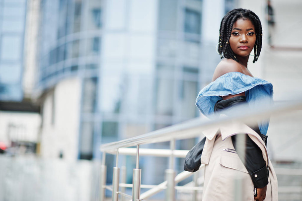 Mulher americana africana atraente com dreads na jaqueta posou perto de grades contra o edifício multistory moderno
. - Foto, Imagem