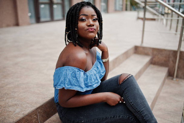 Attractive african american woman with dreads in jeans wear sitting on stairs. - 写真・画像