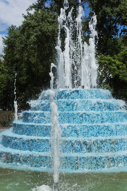 Городской фонтан Фонтан в городском парке в жаркий летний день. Поток воды, капли и яркие брызги воды в красивом городском фонтане. Яркие потоки газированной воды в городском фонтане днем
 - Фото, изображение