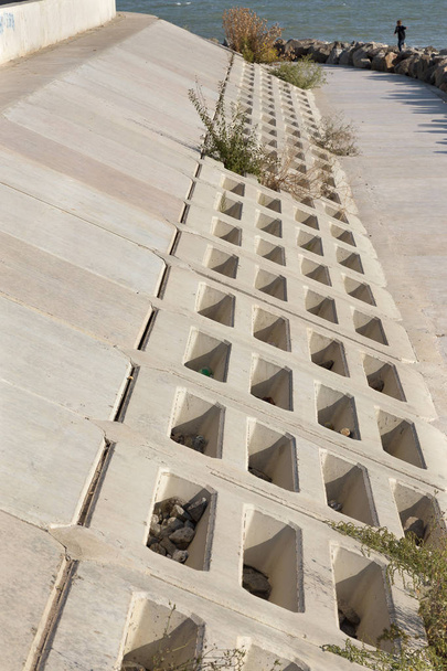 Lähikuva Moderni aallonmurtaja suunnittelu suuria kiviä ja betonilaattoja soluilla erityistä aallonmurtaja suunnittelu. Laituri betonin ja kiven lohkojen rannikon suojelemiseksi. Rannikon konsolidointi
 - Valokuva, kuva