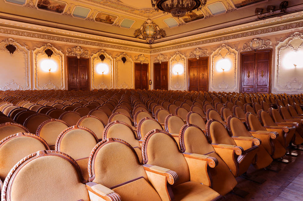 Traditional classical royal richly decorated round wooden ancient plush dark velvet opera chairs for viewers, places in cinemas in curved row with decorative quaint carpet. hall with line of chairs - Photo, Image