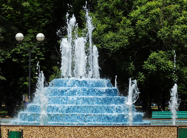 市内の噴水。夏の暑い日に公園の噴水。美しい街の噴水の水の明るい水しぶき、滴水のストリーム。日市泉に輝く水の明るいストリーム - 写真・画像