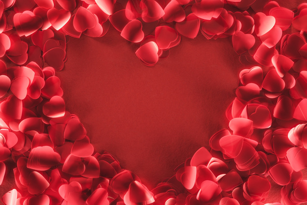κάτοψη του καρέ όμορφο σχήμα καρδιάς από διακοσμητικά πέταλα σε κόκκινο φόντο  - Φωτογραφία, εικόνα