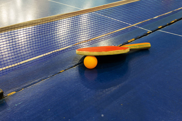 Настільний тенісний пінг-понг. Настільна тенісна ракетка з пластиковим м'ячем для пінг-понг на ігровому столі. Спортивний фон настільної спортивної гри в пінг-понгу. Тенісна ракетка, тенісний м'яч на ігровому столі
 - Фото, зображення