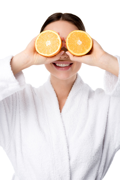 smiling woman in white bathrobe holding oranges in front of face isolated on white - Foto, Imagem