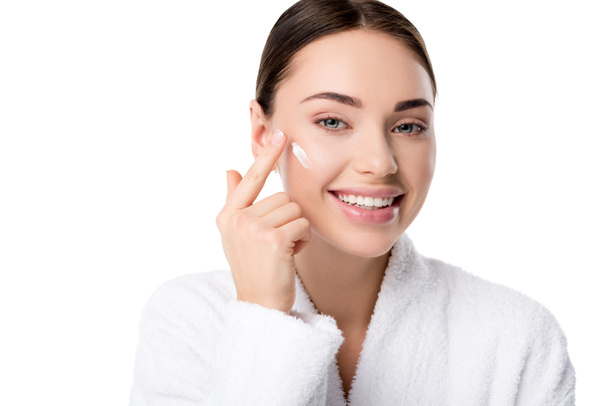 beautiful woman applying moisturizing face cream and looking at camera isolated on white - Photo, Image